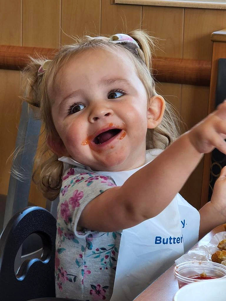 Athena is registered to the contest to win money with this photo: baby, baby_toddler_clothing, blond, cheek, child, comfort_food, cooking, face, food_craving, fun, gesture, hand, happy, iris, joy, person, skin, smile, t_shirt, tableware