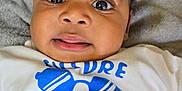Adriel is registered to the contest to win money with this photo: baby, blanket, blue, child, clothing, cute, expression, eyes, fabric, face, graphic, indoors, infant, laying, portrait, shirt, sunglasses, text, tongue, white