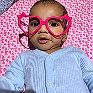 Adhyan is registered to the contest to win money with this photo: baby, infant, glasses, heart_shaped_glasses, pink, blue_clothing, blanket, patterned_blanket, cute, close_up, portrait, child, face, eyes, mouth, onesie, lying_down, indoor, soft_lighting, expression