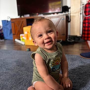 Audis joined the competition — help win amazing prizes! baby, child, smile, sitting, carpet, green_shirt, indoor, living_room, furniture, wood_floor, toy, cute, portrait, happy, infant, person, face, arm, diaper, bracelet