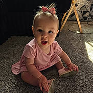 Lucy joined the competition — help win amazing prizes! baby, child, pink_dress, bow, carpet, indoor, sitting, shoe, hand, footwear, curious, light, shadow, floor, person, young_child, expression, playful, home, furniture