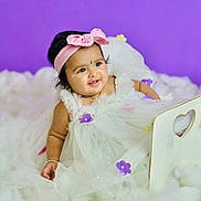 Druvika is registered to the contest to win money with this photo: baby, child, infant, dress, white_dress, headband, pink_bow, purple_flowers, smiling, portrait, fluffy_surface, purple_background, cute, adorable, jewelry, bracelet, studio_photo, sitting, happy, young_child