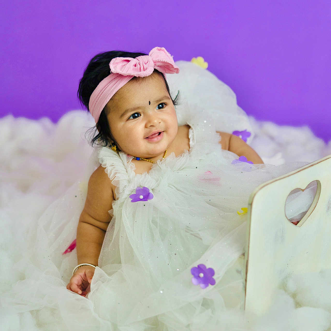 Druvika is registered to the contest to win money with this photo: adorable, baby, bracelet, child, cute, dress, fluffy_surface, happy, headband, infant, jewelry, pink_bow, portrait, purple_background, purple_flowers, sitting, smiling, studio_photo, white_dress, young_child