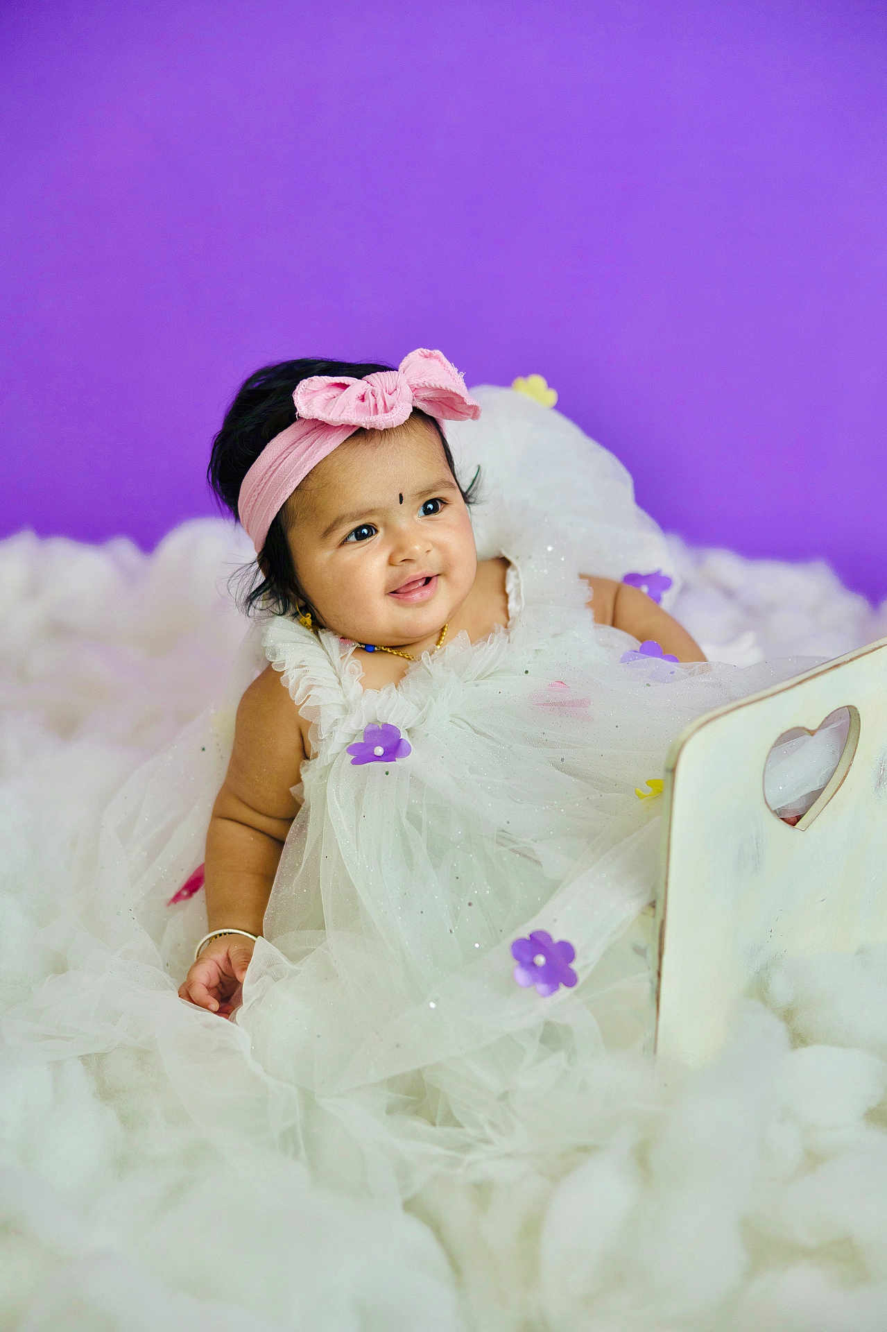 Druvika is registered to the contest to win money with this photo: baby, child, infant, dress, white_dress, headband, pink_bow, purple_flowers, smiling, portrait, fluffy_surface, purple_background, cute, adorable, jewelry, bracelet, studio_photo, sitting, happy, young_child