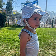 Aymila a rejoint le concours — aidez-le/la à gagner de superbes lots ! toddler, child, outdoor, grass, sunhat, striped_clothing, summer, daylight, portrait, side_view, young_child, curious, solemn, greenery, nature, playground, barefoot, necklace, person, sunshine