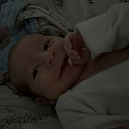 Jasiah is registered to the contest to win money with this photo: baby, infant, smiling, blanket, bed, sleeping_area, hand, face, clothing, soft, patterned, cute, young_child, lying_down, indoor, comfort, warm, closeup, nursery, rest