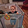 toddler, child, baby, smiling, standing, playpen, toy, colorful_toy, indoors, living_room, dog, sleeping_dog, recliner, wood_floor, rug, halloween, pumpkin, television, furniture, portrait