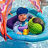 baby, child, infant, swimming_pool, float, inflatable_float, water, rubber_duck, beach_ball, swimwear, swim_cap, smiling, sitting, outdoor, colorful, poolside, toy, portrait, summer, recreation