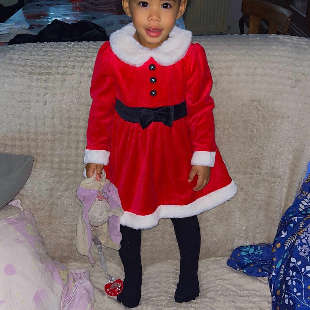 Maianna participe au concours pour gagner de l'argent avec cette photo : black_tights, blanket, chair, child, couch, cozy, curly_hair, curtains, furniture, girl, hair_bows, holiday_outfit, home, indoor, pacifier, red_dress, smile, toy, window, wooden_cabinet