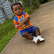 Marquin joined the competition — help win amazing prizes! child, toddler, pajamas, paw_patrol, sitting, sidewalk, outdoor, grass, fence, curly_hair, white_shoes, orange_shirt, blue_shorts, concrete, casual, young_child, person, daylight, greenery, expression