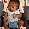 baby, blanket, brown_skin, car_seat, child, clothing, curly_hair, cushion, facial_expression, floral_pattern, hands, indoors, infant, nike, onesie, photography, portrait, safety_labels, sitting, vehicle