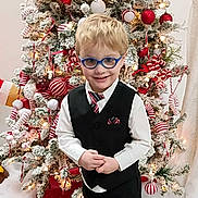 Leviticus is registered to the contest to win money with this photo: boy, celebration, child, christmas_tree, decoration, festive, glasses, green, happy, holiday, indoor, lights, ornaments, portrait, red, smile, tie, vest, white, winter