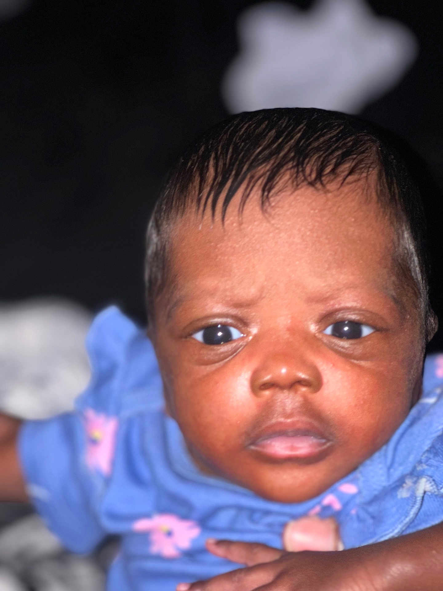 Nadia is registered to the contest to win money with this photo: baby, infant, face, closeup, blue_clothing, pink_flowers, skin, eyes, hand, portrait, child, cute, young, expression, person, indoors, human, head, newborn, baby_girl