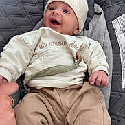 Marley participe au concours pour gagner de l'argent avec cette photo : baby, infant, child, knitted_hat, smiling, happy, quilted_blanket, clothing, beige_pants, cream_sweater, hand, portrait, cute, cozy, indoor, fabric, face, person, sitting, warm