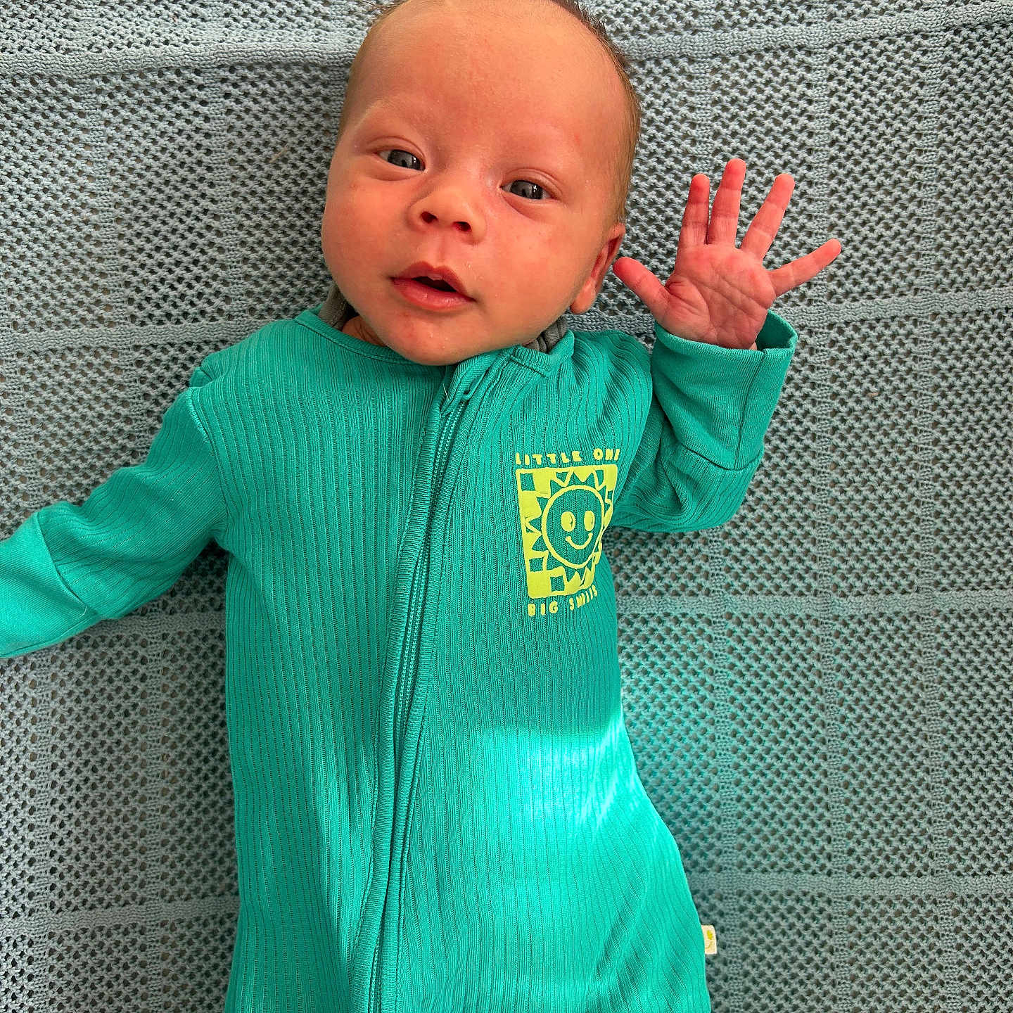 Hunter joined the competition — help win amazing prizes! baby, blanket, child, clothing, cute, expression, face, hand_wave, happy, indoor, infant, lying_down, newborn, onesie, person, portrait, small_hand, smiling, teal, texture
