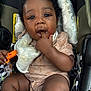 baby, child, car_seat, infant, cute, fingers_in_mouth, bib, clothing, curly_hair, seatbelt, texture, face, person, skin, hand, legs, black_hair, expression, indoor, sitting