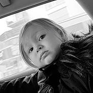 Lya a rejoint le concours — aidez-le/la à gagner de superbes lots ! child, toddler, coat, blanket, car_interior, window, face, portrait, black_and_white, fur_collar, curious, young_child, clothing, seat, person, indoor, expression, soft_texture, automobile, travel