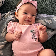 Riley is registered to the contest to win money with this photo: baby, infant, child, smiling, portrait, pink_outfit, headband, bow, little_sister, lying_down, cushion, blanket, indoors, cozy, happy, face, hands, arms, legs, photography