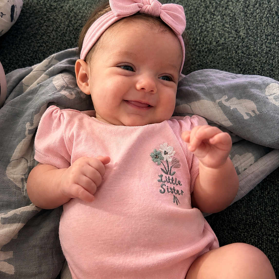 Riley is registered to the contest to win money with this photo: baby, infant, child, smiling, portrait, pink_outfit, headband, bow, little_sister, lying_down, cushion, blanket, indoors, cozy, happy, face, hands, arms, legs, photography