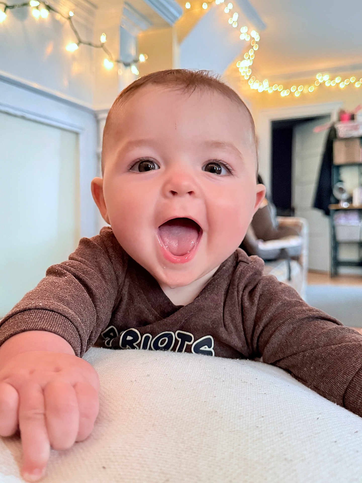 Beau joined the competition — help win amazing prizes! baby, child, smiling, happy, indoor, face, person, clothing, hand, expression, cute, infant, tongue, eyes, light, string_lights, background, furniture, home, cozy