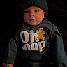 Carter is registered to the contest to win money with this photo: baby, child, hat, knit_hat, gingerbread_man, dark_background, sweater, clothing, cute, portrait, infant, childwear, smiling, face, looking, hands, cozy, indoors, person, warm