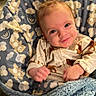 baby, infant, smiling, child, blanket, baby_seat, clothing, indoors, cute, face, portrait, soft_texture, pattern, comfort, happy, young_child, cozy, blue, warm_light, expression