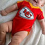 baby, infant, smiling, red_onesie, sports_logo, kansas_city_chiefs, blanket, soft_texture, wooden_sign, five_months, happy, chubby_cheeks, laying_down, cute, portrait, child, skin, face, hand, foot