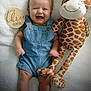 baby, infant, smile, denim_overalls, stuffed_animal, giraffe_toy, blanket, wooden_sign, happy, cute, child, portrait, lying_down, soft_texture, clothing, baby_girl, baby_boy, infant_face, playful, joyful