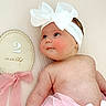 baby, infant, headband, bow, pink, skirt, rosy_cheeks, blue_eyes, plush, soft_texture, decorative_plaque, ribbon, cute, portrait, child, newborn, lying_down, skin, closeup, adorable
