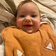 Fabio a rejoint le concours — aidez-le/la à gagner de superbes lots ! baby, infant, child, face, smile, eyes, cheeks, blanket, bedding, pillow, onesie, orange_clothing, embroidered_detail, bed, happy, closeup, portrait, hair, skin, mouth