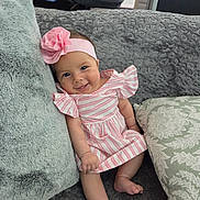 Sarahi is registered to the contest to win money with this photo: baby, girl, smiling, pink_headband, striped_dress, couch, pillows, cozy, indoor, cute, infant, child, happy, portrait, relaxing, soft_texture, home, seated, comfortable, adorable