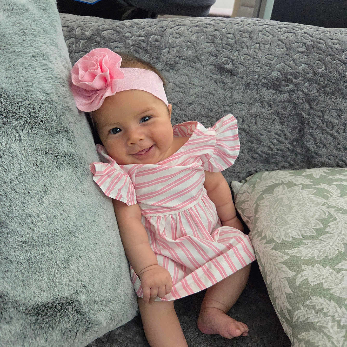 Sarahi is registered to the contest to win money with this photo: baby, girl, smiling, pink_headband, striped_dress, couch, pillows, cozy, indoor, cute, infant, child, happy, portrait, relaxing, soft_texture, home, seated, comfortable, adorable