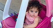 Isabel is registered to the contest to win money with this photo: baby, child, toddler, toy_car, pink, outdoor, sitting, portrait, face, eyes, hair, smiling, striped_shirt, clothing, vehicle, driveway, wheel, plastic, playtime, family
