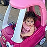 baby, child, toddler, toy_car, pink, outdoor, sitting, portrait, face, eyes, hair, smiling, striped_shirt, clothing, vehicle, driveway, wheel, plastic, playtime, family