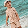 child, boy, hat, beach, ocean, waves, shorts, shirt, smile, happy, footwear, water, outdoor, summer, sunny, portrait, kids_fashion, vacation, sand, casual_clothing