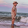 child, beach, ocean, waves, sand, hat, shorts, shirt, footwear, water, sky, sunset, reflection, standing, curious, outdoor, shore, clothing, nature, person