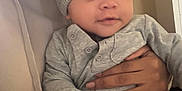 Kingston is registered to the contest to win money with this photo: baby, child, knit_hat, gray_clothing, hand, person, indoor, portrait, smile, cute, infant, human_skin, warm, holding, face, eyes, sitting, cozy, hoodie, adult_hand