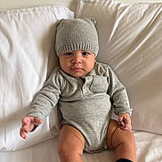 Kingston is registered to the contest to win money with this photo: baby, child, infant, hat, knit_hat, grey_clothing, onesie, sitting, bed, pillows, white_bed, cute, reaching_hand, indoor, cozy, soft_light, portrait, smiling, black_socks, gap_socks
