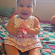 Shaira joined the competition — help win amazing prizes! baby, smiling, headband, white_dress, sitting, bed, quilt, colorful, indoor, child, cute, happy, comb, toys, window, natural_light, skin, feet, hands, infant