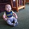 baby, child, bib, carpet, furniture, green_carpet, indoor, living_room, table, wooden_table, couch, plush_couch, clothing, socks, sitting, expression, person, face, cute, home