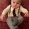 baby, infant, child, hat, pants, couch, red_couch, sitting, looking_at_camera, indoors, cute, clothing, patterned_clothes, footwear, person, portrait, young_child, casual, relaxed, home