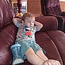 Lakoda is registered to the contest to win money with this photo: toddler, child, sitting, couch, leather, relaxing, indoor, person, shorts, tshirt, cup, sippy_cup, barefoot, furniture, lamp, wood_paneling, living_room, face, expression, casual