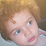 Alina is registered to the contest to win money with this photo: child, curly_hair, face, portrait, close_up, blue_eyes, expression, skin, person, young, indoor, casual_clothing, soft_light, thoughtful, cute, baby, head, toddler, looking_away, pale_skin