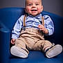baby, child, blue_chair, smiling, suspenders, beige_pants, blue_shirt, happy, portrait, cute, indoor, modern_furniture, seated, infant, clothing, footwear, one_person, young_child, casual_wear, studio_lighting