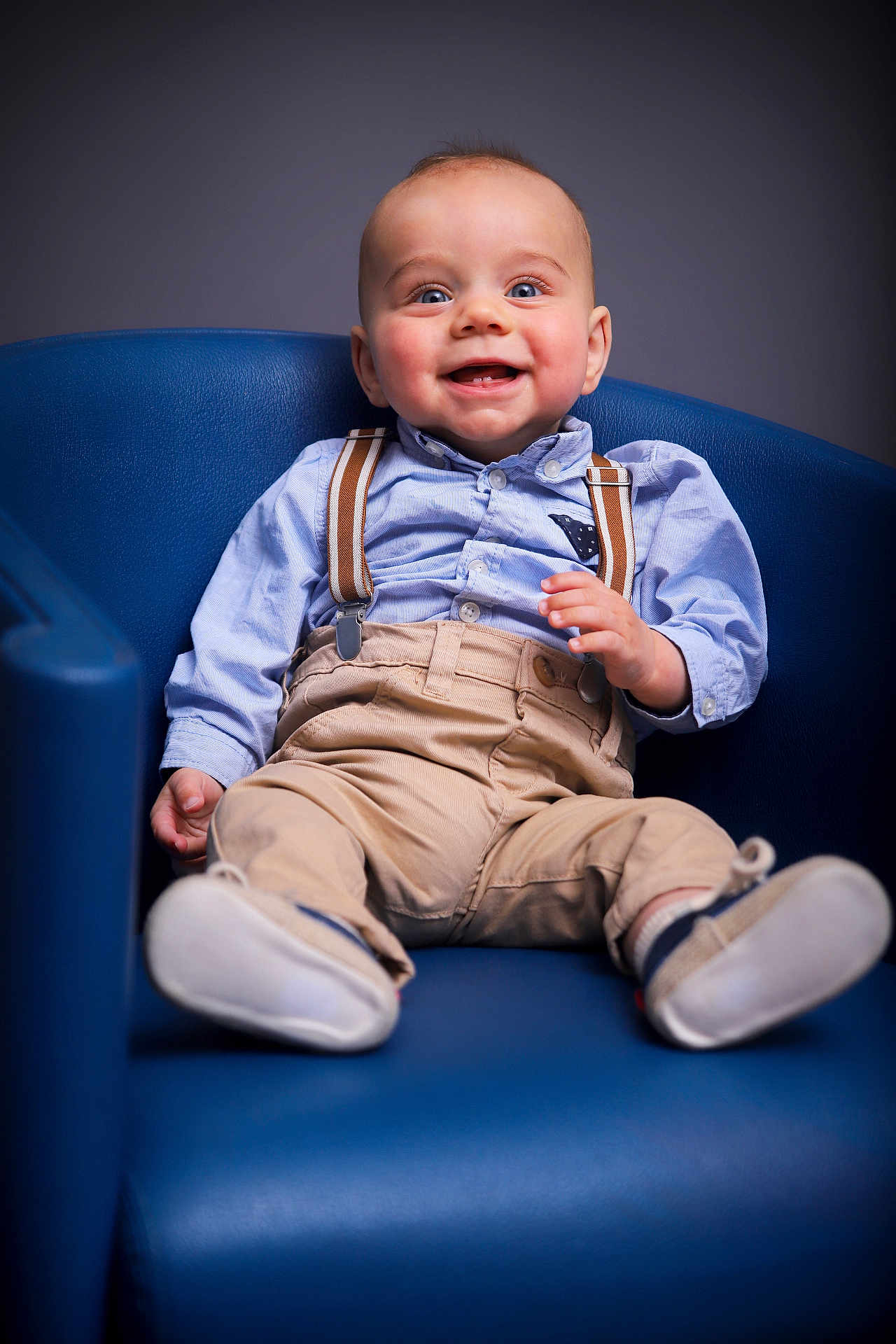 Charles a rejoint le concours — aidez-le/la à gagner de superbes lots ! baby, child, blue_chair, smiling, suspenders, beige_pants, blue_shirt, happy, portrait, cute, indoor, modern_furniture, seated, infant, clothing, footwear, one_person, young_child, casual_wear, studio_lighting