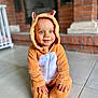 toddler, child, onesie, hood, blue_eyes, smile, indoor, floor, tile, brick_wall, fireplace, crib, cute, cozy, baby, sitting, fuzzy_clothing, hands, portrait, young_child