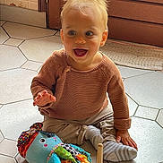 Charles a rejoint le concours — aidez-le/la à gagner de superbes lots ! toddler, child, toy, stuffed_animal, stacking_rings, socks, sweater, floor, tile, indoor, door, glass, happy, smiling, play, person, cute, colorful, daylight, home