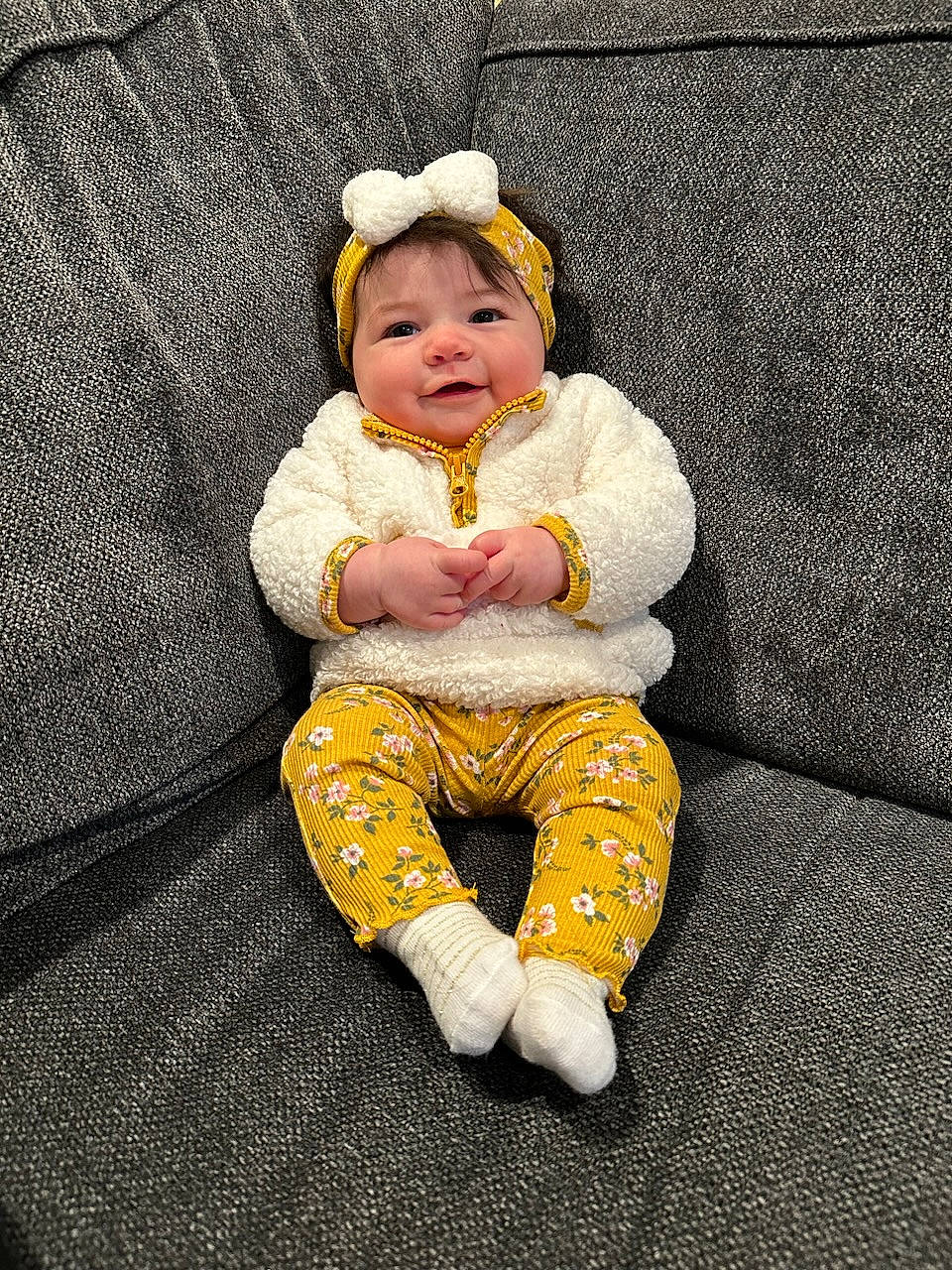 Maisie is registered to the contest to win money with this photo: baby, baby_products, baby_toddler_clothing, beanie, cheek, child, comfort, eye, flooring, grass, happy, headwear, linens, outerwear, pattern, person, portrait_photography, sitting, sleeve, smile