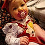 baby, child, pacifier, red_headband, christmas_outfit, reindeer_design, holiday, table_setting, plates, glasses, hand, sitting, cute, indoor, person, festive, white_tights, floral_dress, closeup, face