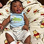 baby, child, infant, smiling, tongue_out, blue_clothing, striped_shorts, white_socks, blanket, winnie_the_pooh, plush_blanket, happy, cute, lying_down, indoors, closeup, soft_texture, playful, young_child, cozy